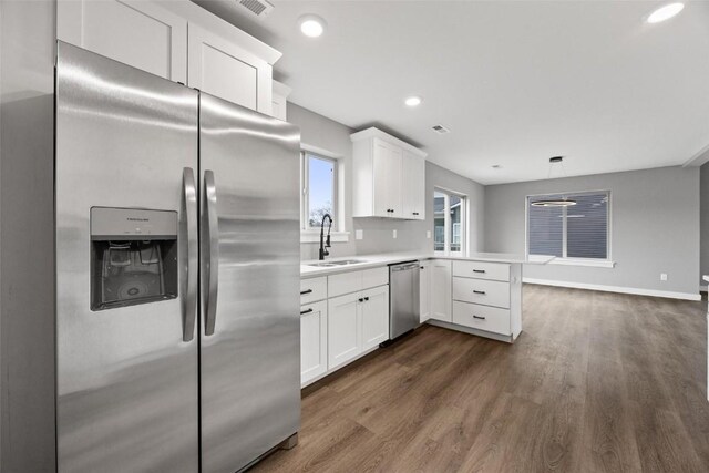 kitchen with sink, kitchen peninsula, hanging light fixtures, white cabinetry, and stainless steel appliances