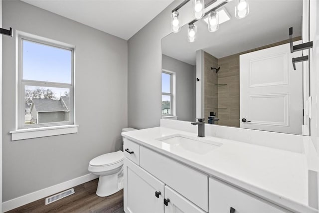 bathroom featuring hardwood / wood-style floors, vanity, toilet, and tiled shower