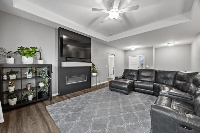 living room featuring a fireplace, a raised ceiling, and dark wood-type flooring