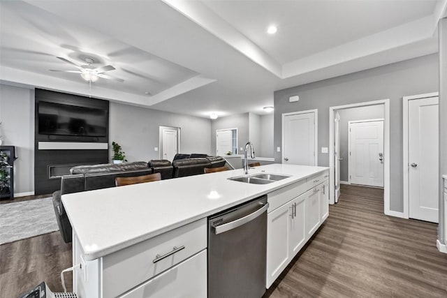 kitchen featuring stainless steel dishwasher, a tray ceiling, a kitchen island with sink, sink, and white cabinets