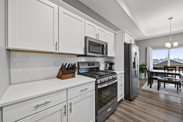 kitchen with white cabinetry, hanging light fixtures, stainless steel appliances, tasteful backsplash, and dark hardwood / wood-style flooring