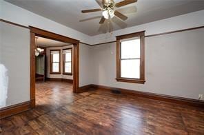 spare room featuring ceiling fan with notable chandelier, a healthy amount of sunlight, and dark wood-type flooring