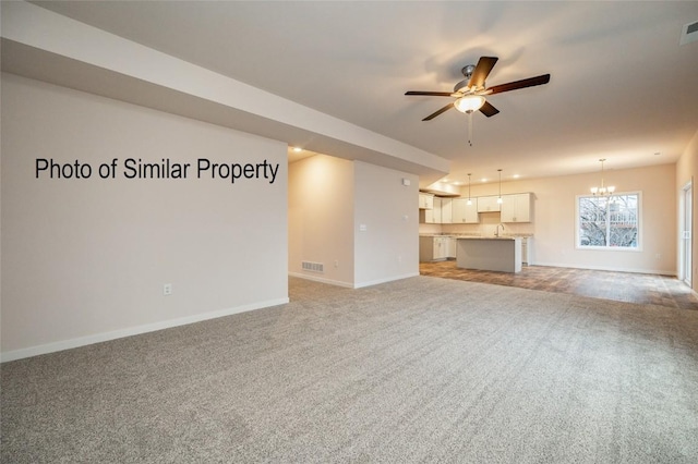 unfurnished living room with ceiling fan with notable chandelier, light colored carpet, and sink