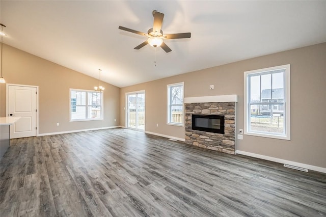 unfurnished living room featuring ceiling fan with notable chandelier, vaulted ceiling, a fireplace, and dark wood-type flooring