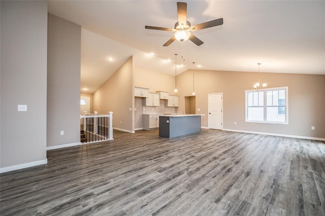 unfurnished living room featuring dark hardwood / wood-style floors, ceiling fan with notable chandelier, and vaulted ceiling