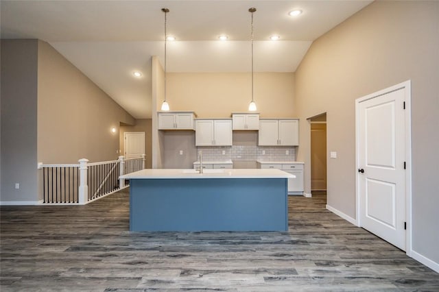 kitchen featuring dark hardwood / wood-style flooring, backsplash, an island with sink, decorative light fixtures, and white cabinets