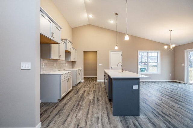 kitchen with pendant lighting, a kitchen island with sink, dark wood-type flooring, an inviting chandelier, and tasteful backsplash