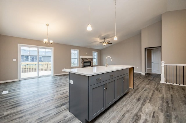 kitchen featuring vaulted ceiling, sink, decorative light fixtures, a center island with sink, and gray cabinets