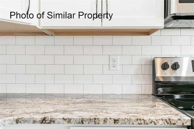 kitchen with white cabinetry, stove, light stone countertops, and backsplash