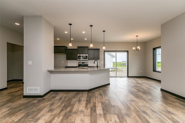 kitchen featuring pendant lighting, an inviting chandelier, sink, light stone countertops, and appliances with stainless steel finishes