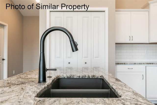 room details with backsplash, light stone countertops, sink, and white cabinets