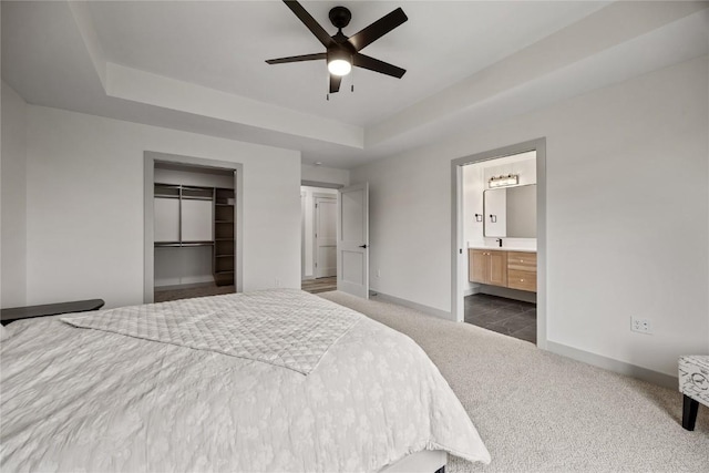 bedroom with connected bathroom, a raised ceiling, dark colored carpet, baseboards, and a spacious closet