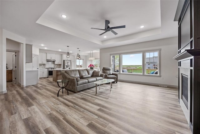 living room featuring recessed lighting, a tray ceiling, ceiling fan, and light wood-style floors