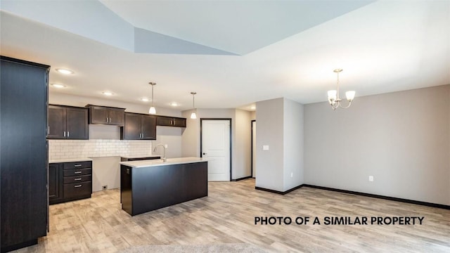 kitchen featuring backsplash, a center island with sink, vaulted ceiling, and hanging light fixtures