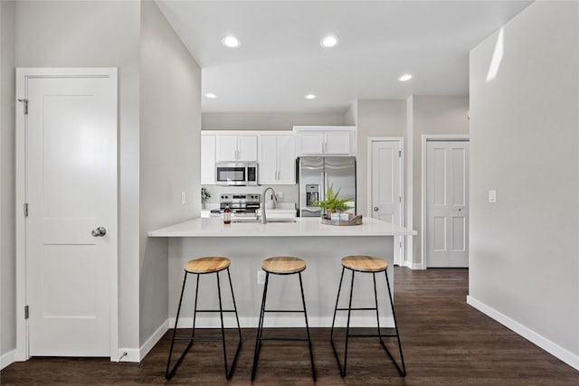 kitchen with kitchen peninsula, a kitchen breakfast bar, stainless steel appliances, and white cabinetry