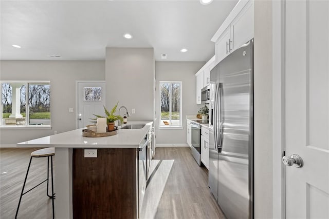 kitchen featuring white cabinets, a center island with sink, sink, appliances with stainless steel finishes, and a kitchen bar