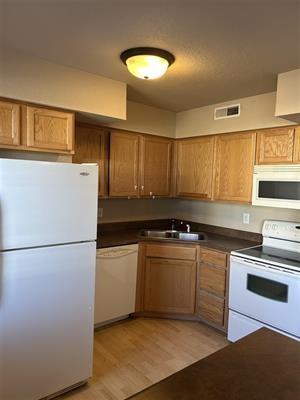 kitchen with light wood-type flooring, white appliances, and sink