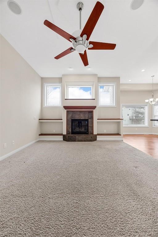 unfurnished living room with carpet flooring, ceiling fan with notable chandelier, and a fireplace