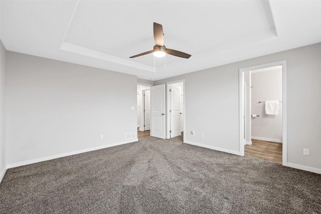 unfurnished bedroom featuring a tray ceiling, ceiling fan, a spacious closet, carpet floors, and a closet