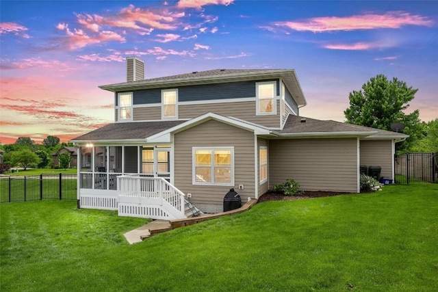 back house at dusk featuring a sunroom and a lawn