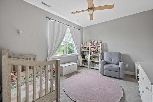 carpeted bedroom with ceiling fan and a crib