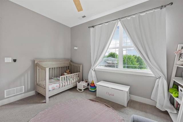 bedroom with light colored carpet, a nursery area, and ceiling fan