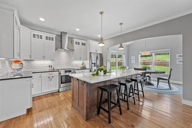 kitchen with white cabinetry, wall chimney range hood, an island with sink, and appliances with stainless steel finishes