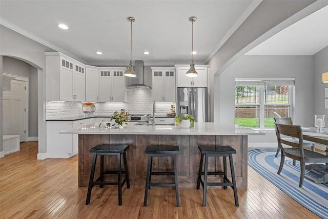 kitchen featuring white cabinets, wall chimney range hood, hanging light fixtures, decorative backsplash, and appliances with stainless steel finishes