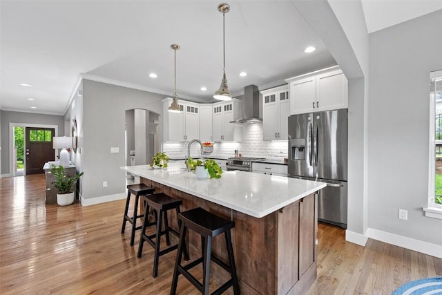 kitchen featuring a kitchen island with sink, white cabinets, wall chimney exhaust hood, light stone countertops, and appliances with stainless steel finishes