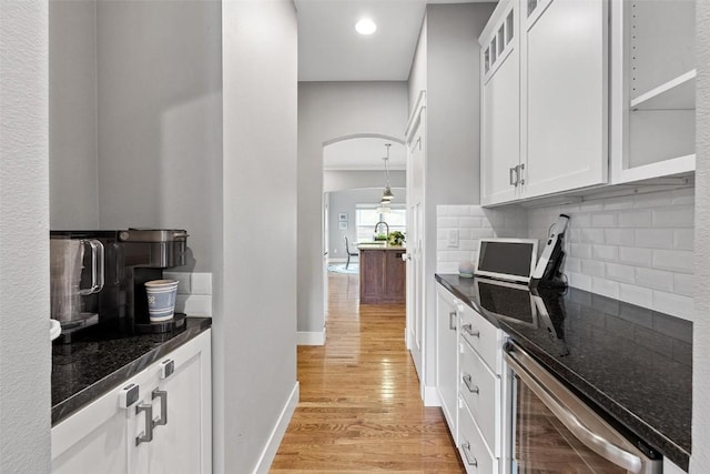 kitchen with backsplash, dark stone counters, light wood-type flooring, white cabinetry, and beverage cooler