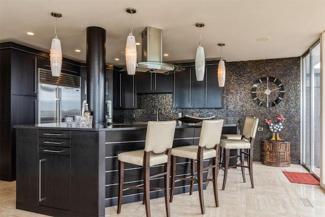 kitchen featuring tasteful backsplash, stainless steel built in refrigerator, island range hood, decorative light fixtures, and a kitchen island