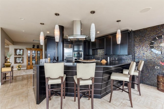 kitchen featuring a kitchen breakfast bar, decorative backsplash, wall chimney range hood, and hanging light fixtures