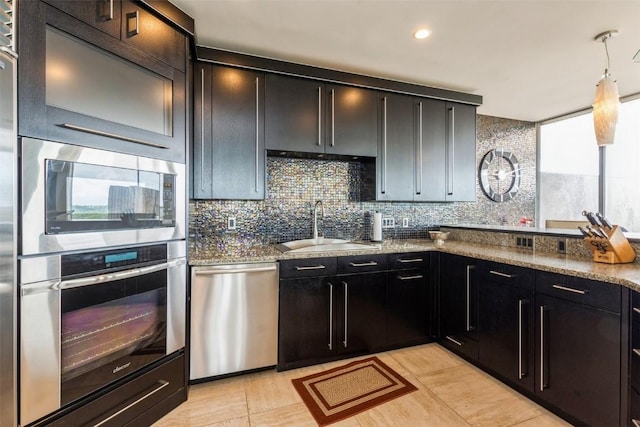 kitchen featuring stone counters, sink, hanging light fixtures, stainless steel appliances, and decorative backsplash