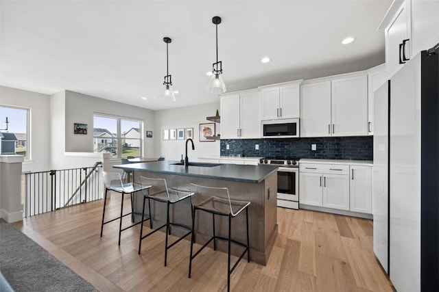 kitchen featuring white appliances, a kitchen island with sink, a healthy amount of sunlight, sink, and white cabinetry