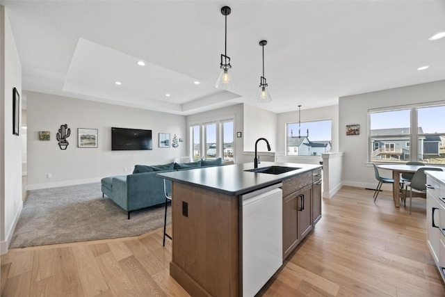 kitchen with a raised ceiling, dishwasher, an island with sink, and sink