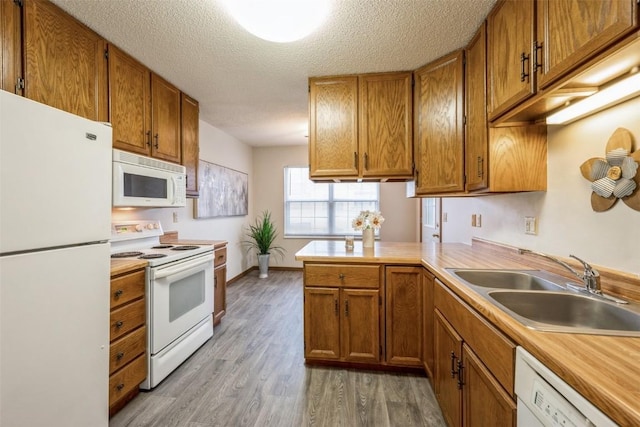 kitchen with white appliances, sink, a textured ceiling, light hardwood / wood-style floors, and kitchen peninsula