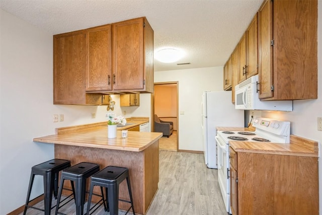 kitchen with a textured ceiling, a breakfast bar, white appliances, and kitchen peninsula