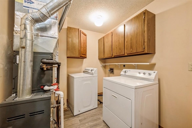 clothes washing area featuring cabinets, washing machine and dryer, heating unit, light hardwood / wood-style floors, and a textured ceiling