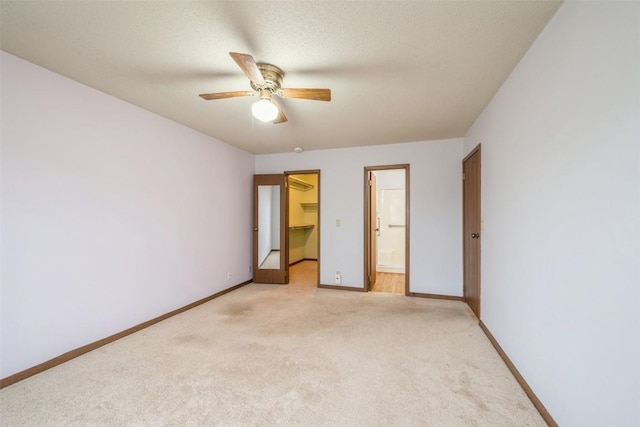 unfurnished bedroom featuring light carpet, ensuite bathroom, a walk in closet, ceiling fan, and a closet