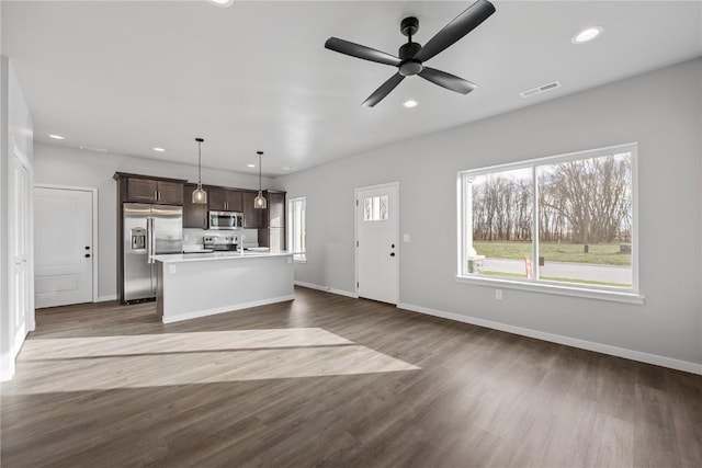 kitchen featuring appliances with stainless steel finishes, dark brown cabinetry, a kitchen island with sink, ceiling fan, and decorative light fixtures