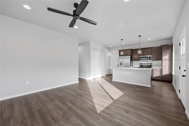 kitchen featuring a kitchen island with sink, hanging light fixtures, appliances with stainless steel finishes, dark brown cabinets, and dark hardwood / wood-style flooring