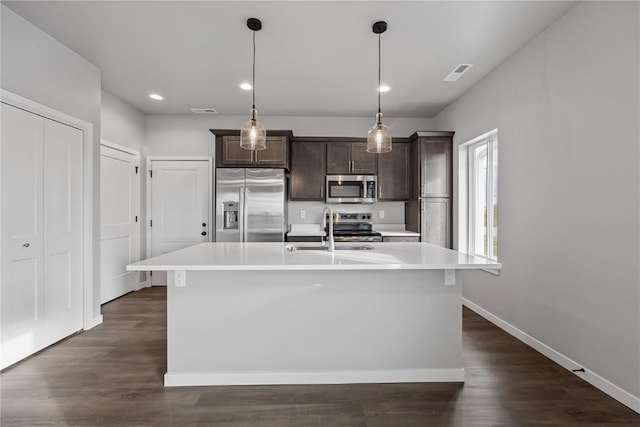 kitchen featuring a center island with sink, sink, decorative light fixtures, appliances with stainless steel finishes, and dark brown cabinets