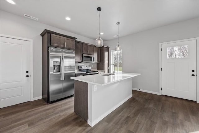 kitchen featuring dark brown cabinetry, sink, hanging light fixtures, stainless steel appliances, and a kitchen island with sink