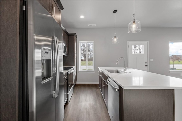 kitchen with dark brown cabinetry, sink, an island with sink, pendant lighting, and appliances with stainless steel finishes