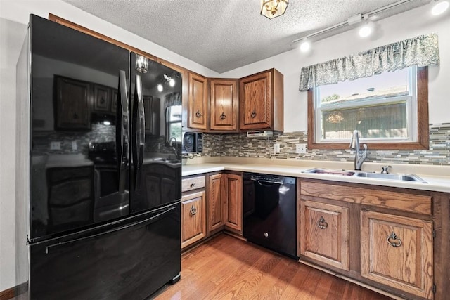 kitchen featuring backsplash, a textured ceiling, sink, black appliances, and light hardwood / wood-style floors