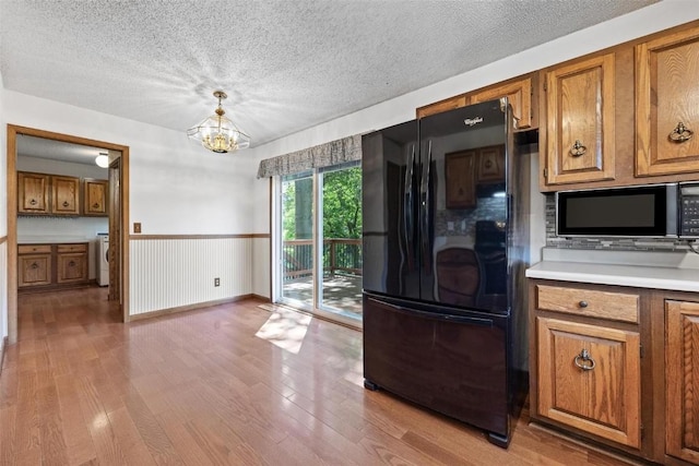 kitchen featuring a textured ceiling, black appliances, pendant lighting, a notable chandelier, and light hardwood / wood-style floors