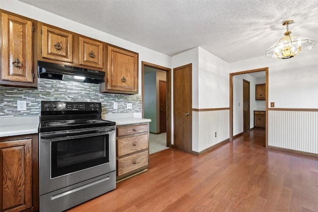 kitchen with stainless steel range with electric cooktop, an inviting chandelier, hanging light fixtures, tasteful backsplash, and wood-type flooring