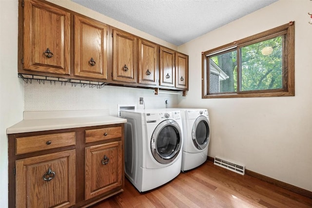 clothes washing area with hardwood / wood-style floors, washer and dryer, cabinets, and a textured ceiling