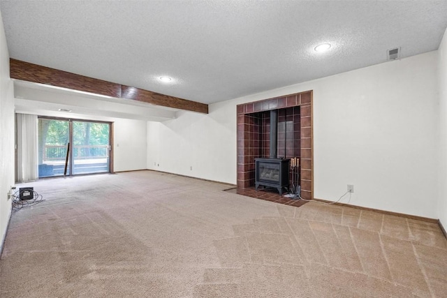 unfurnished living room featuring beam ceiling, a wood stove, carpet flooring, and a textured ceiling