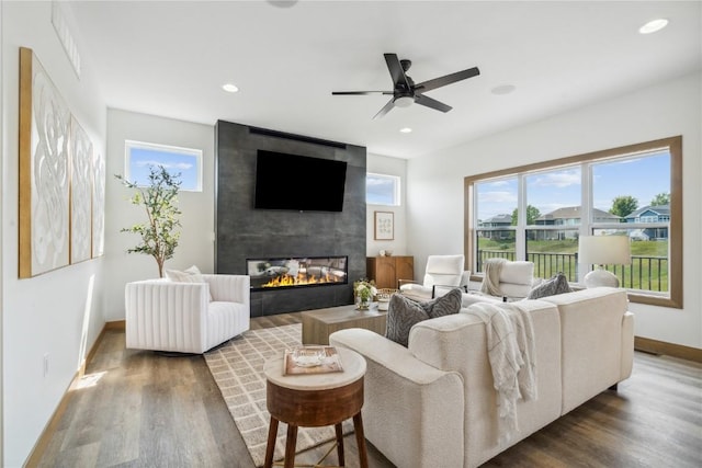 living room with dark hardwood / wood-style flooring, ceiling fan, and a large fireplace